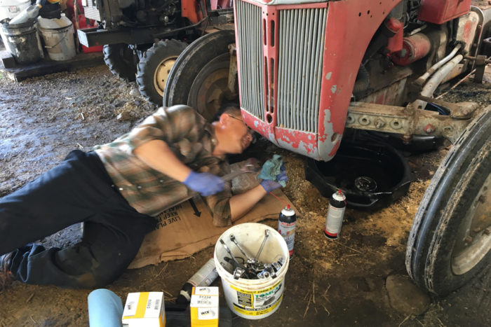 Blia and Phua's son Boun changes the oil in Thao's Garden's tractor.