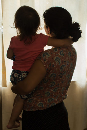 Isabel*, who worked in pork processing, holds her toddler daughter in their trailer home in Lenoir County after receiving a food donation. Photo by Justin Cook.