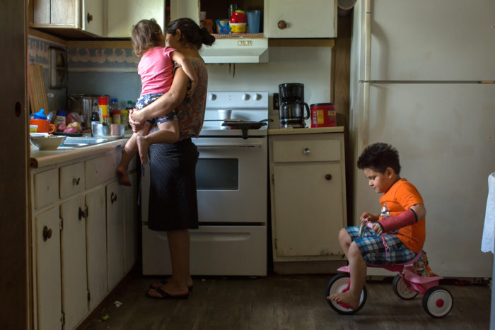 Isabel*, who worked in pork processing, cooks for her children in their trailer home in Lenoir County after receiving a food donation. (Photo by Justin Cook.)