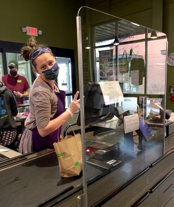 A co-op worker behind a plexiglas shield. Photo courtesy of Green Top Grocery.