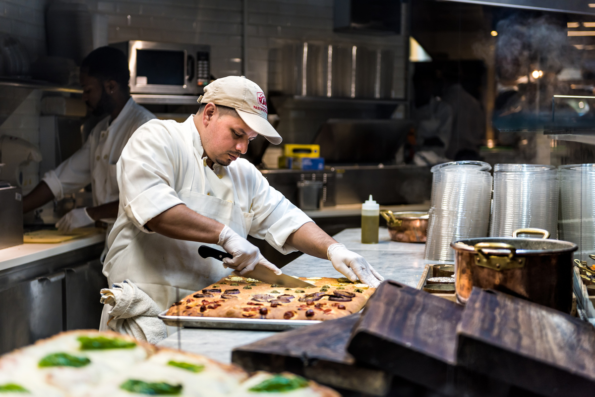 A restaurant worker slices focaccia bread in the kitchen of a restaurant