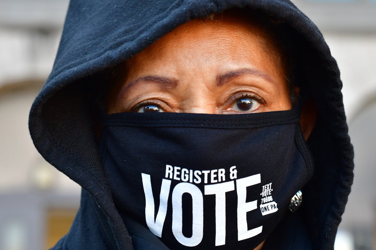 Site manager Eileen Bowman wears a "REGISTER & VOTE" mask as long lines of voters wait to cast early voting ballots at Roxborough High School on October 17, 2020 in Philadelphia, Pennsylvania. (Photo by Mark Makela/Getty Images)