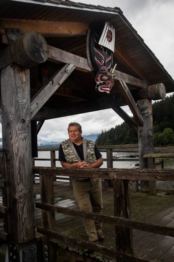 Ho'miska̱nis, Don Svanvik, a traditional carver, and hereditary chief and current elected Chief of Council of the ‘Na̱mg̱is First Nation under a carving he made on the waterfront in Alert Bay.