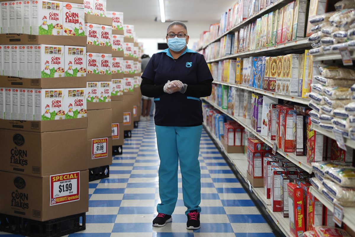 A frontline supermarket worker poses for a picture as she wears a mask and gloves while working at a Miami supermarket.