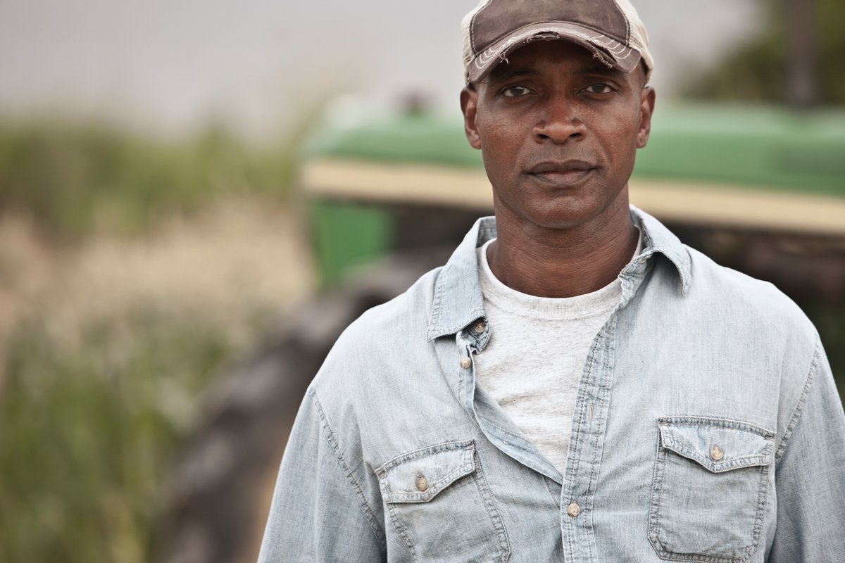 a black farmer standing in front of a tractor.