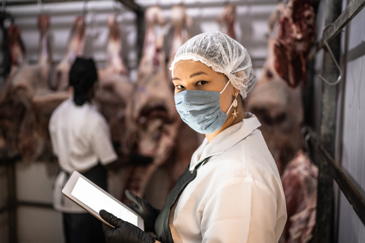 Portrait of female butcher using digital tablet with face mask at a meatpacking plant