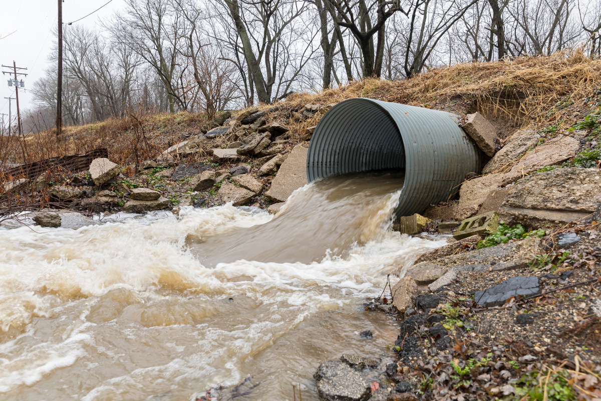 Closeup motion blur of storm water runoff flowing through metal drainage culver under road. January storms brought heavy rain and flash flooding to Illinois - stock photo