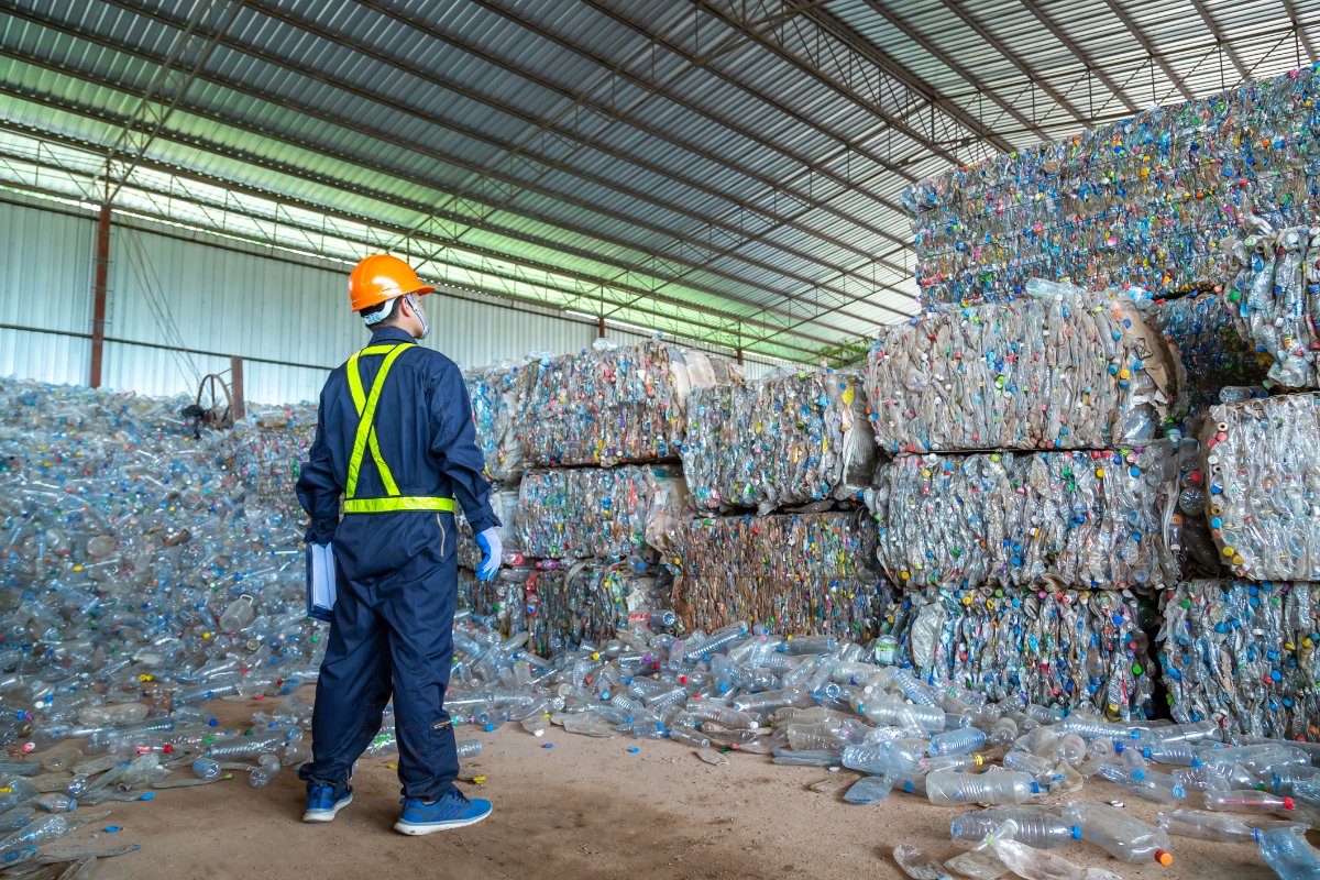 a worker stands in front of a massive pile of plastic bottles destined to be recycled