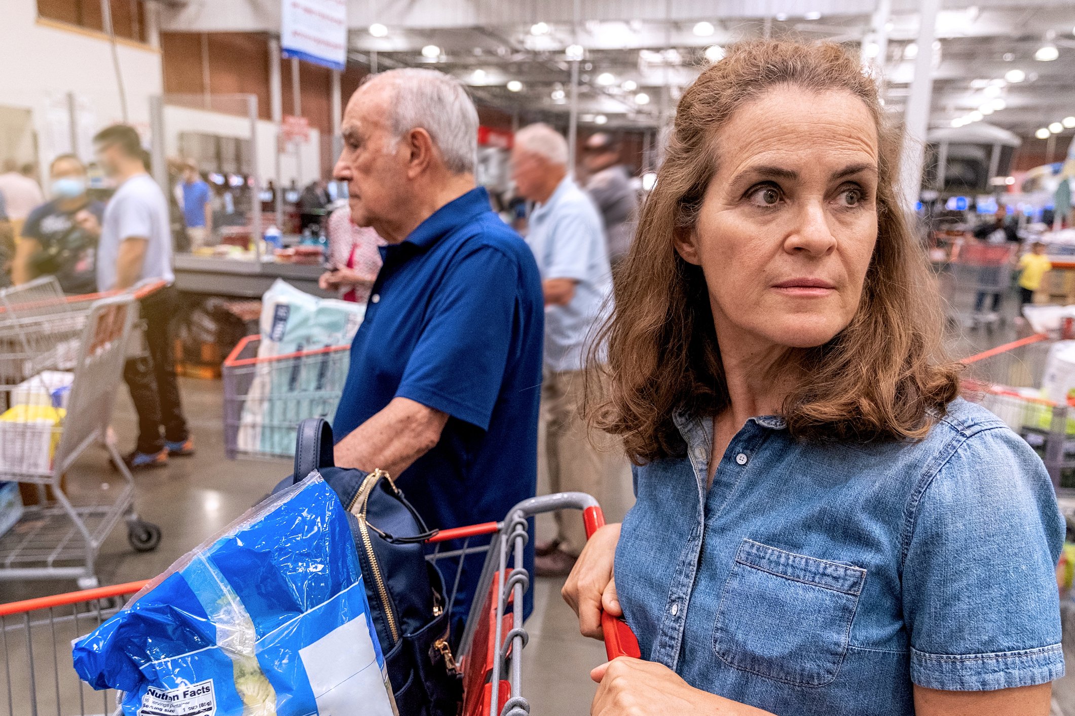 An older woman looks worried while waiting to pay for her food purchases at a supermarket.