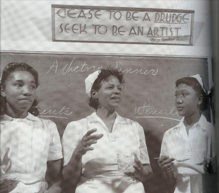 A group of Black women lead a cooking class; a banner above the chalkboard reads, "Cease to be a drudge, Seek to be an artist," credited to Mary McLeod Bethune. (Photo courtesy of The Jemima Code and the Center for Documentary Studies at Duke University)