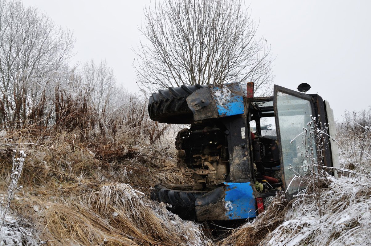 A tractor rollover accident with a farm tractor on its side in a ditch.