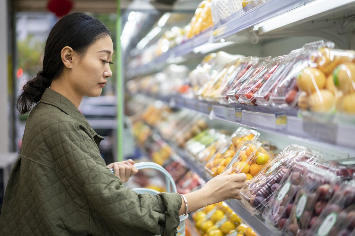 a woman shopping for produce surrounded by plastic